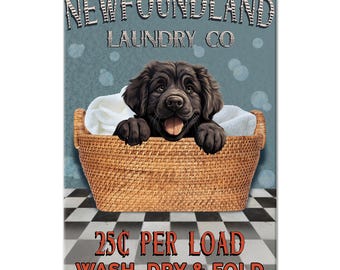 May include: A rectangular metal sign featuring a black Newfoundland puppy inside a woven wicker laundry basket filled with white towels. The text reads NEWFOUNDLAND LAUNDRY CO at the top and 25¢ PER LOAD WASH, DRY & FOLD at the bottom.