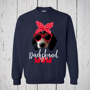 May include: Navy blue sweatshirt with a graphic of a dachshund wearing red sunglasses and a red and white polka dot bandana. The text "Dachshund Mom" is printed in white below the dog.