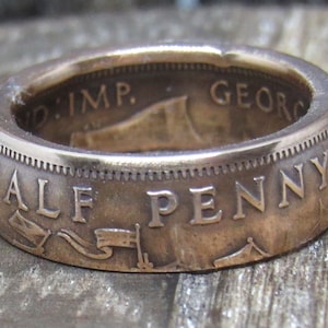 May include: A copper-colored ring made from a half penny coin. The ring features the inscription "HALF PENNY" and the words "GEORG" and "IMP." on the inside of the band.