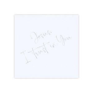 May include: A square, white card with the words "Jesus, I Trust in You" written in a delicate, cursive font. The text is a light, silvery color, contrasting against the clean white background.