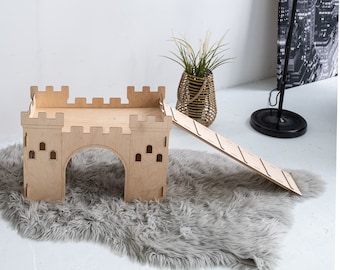 May include: A wooden castle-shaped pet bed with a ramp leading up to the top. The bed is made of natural wood and has a light brown finish. The ramp is also made of wood and has a light brown finish. The bed is sitting on a gray fluffy rug.