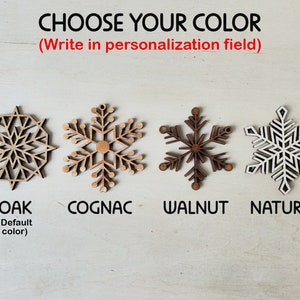 May include: Four wooden snowflake ornaments in different wood stains: oak, cognac, walnut, and natural. The text "CHOOSE YOUR COLOR (Write in personalization field)" is above the ornaments.