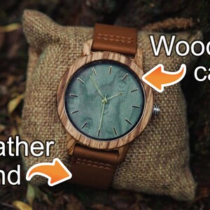 May include: A wooden wristwatch with a brown leather band. The watch face has a green background with gold-colored hands and markings. The text "Wooden case" is written above the watch and "Leather band" is written below the watch.