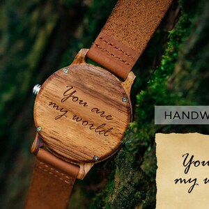 May include: A wooden wristwatch with a brown leather band. The watch face is engraved with the words "You are my world".