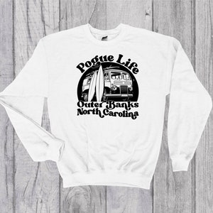Puede incluir: Sudadera blanca de manga larga con un estampado gráfico negro de una furgoneta vintage con tablas de surf y el texto "Pogue Life Outer Banks North Carolina".