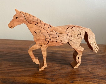 May include: A wooden horse puzzle with intricate cutouts. The horse is standing on all four legs with its head held high. The puzzle is made of light brown wood and has a natural finish.