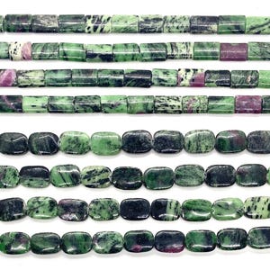 May include: Multiple strands of polished zoisite beads featuring a mix of vibrant green, deep black, and magenta-pink inclusions. The beads are shaped into uniform rectangles and flattened ovals, arranged in horizontal rows against a white background.