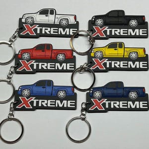 May include: Five keychains featuring different coloured trucks with the word "XTREME" on each. The trucks are white, red, yellow, blue and black.
