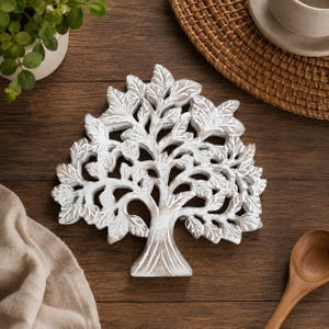 May include: A decorative wooden trivet shaped like a tree with a white distressed finish. The cutout design features intricate branches and leaves, showcasing the natural wood grain underneath the white paint in a flat, symmetrical composition.