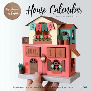 Puede incluir: Un calendario de casa de papel con el texto "House Calendar" y "2026". El calendario es rosa, beige y marrón, con la fecha del 14 de julio mostrada. El diseño incluye flores, ventanas y una farola. El texto "DIGITAL SVG FILE" también es visible.