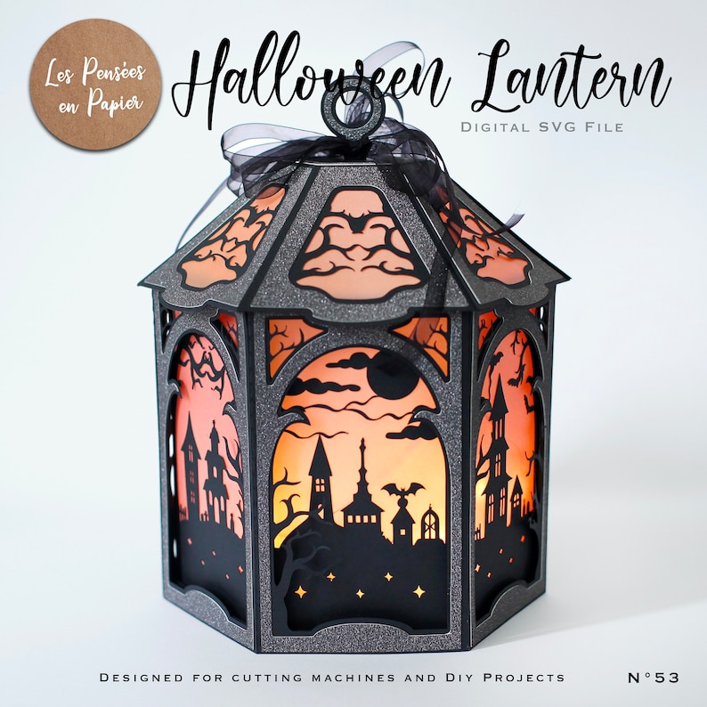 Puede incluir: Una linterna hexagonal hecha de cartulina gris oscuro con purpurina y recortes intrincados de una casa encantada, murci&eacute;lagos y una luna. Los paneles est&aacute;n iluminados con un brillo naranja y una cinta negra est&aacute; atada al anillo superior.