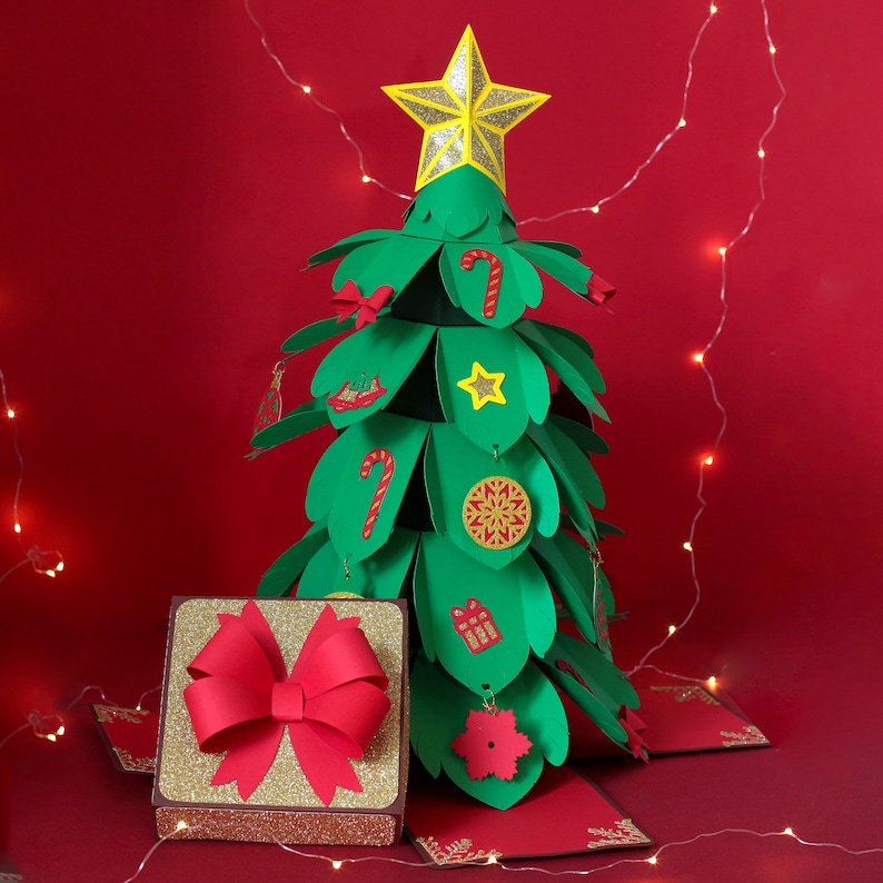 May include: A green paper Christmas tree with a yellow star on top. The tree is decorated with red and white candy canes, a red bow, and other festive details. A gold gift box with a red bow sits in front of the tree.