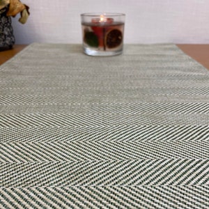 May include: A green and white chevron patterned table runner. The runner is made of a woven material and has a subtle sheen.