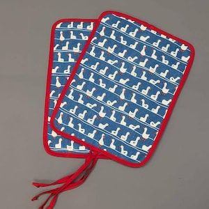 May include: A pair of blue and white cotton pot holders with a red trim and a pattern of white geese on a blue background. The pot holders have red ties.