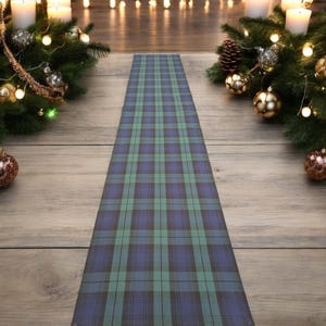 May include: A green, blue and black tartan table runner. The runner is on a wooden floor with Christmas decorations on either side.