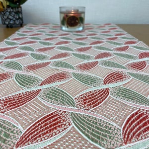 May include: A red and green table runner with a geometric pattern of overlapping circles. The runner is made of a woven fabric with a subtle texture.