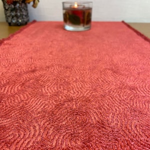 May include: A red table runner with a textured, wavy pattern. The runner is made of a soft, plush fabric.