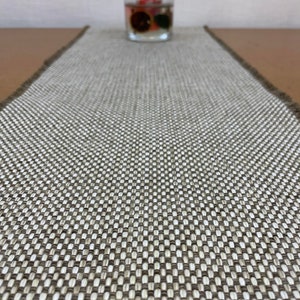 May include: A brown and white woven table runner with a subtle checkered pattern. The runner is made of a natural material and has a slightly textured surface.
