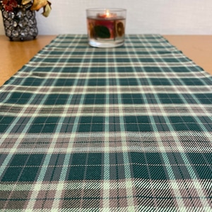 Puede incluir: Un camino de mesa de tejido a cuadros verde, marrón y blanco. El camino de mesa está hecho de un tejido tejido y tiene un brillo sutil.