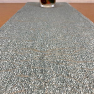 May include: A teal blue table runner with a subtle woven pattern. The runner has a textured surface and a slightly shimmery finish.