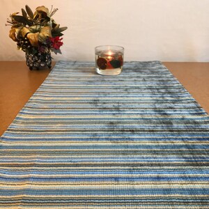 May include: A blue and beige striped table runner with a candle in a glass jar on top of it.