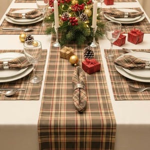May include: A dining table set for six with a white tablecloth and a brown, tan, and red plaid table runner and matching placemats. Each place setting includes a white plate, a plaid napkin with a silver ring, a glass, and silverware.