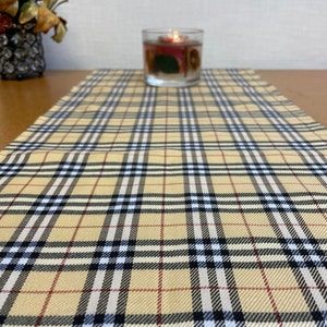 May include: A beige and black plaid table runner with a red and white stripe pattern. The runner is made of a woven fabric and has a soft, textured feel.