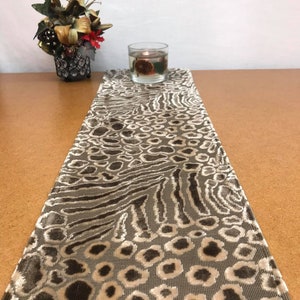 Op de afbeelding: Een beige en bruine tafelrunner met een luipaardprint. De runner is gemaakt van een zachte, fluweelachtige stof.