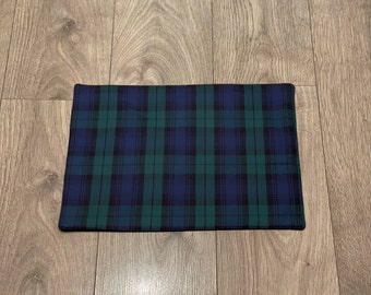 May include: A rectangular placemat with a classic plaid pattern in shades of navy blue, forest green, and black. The fabric appears to be a woven material, and the edges are neatly finished. The placemat is designed for dining.