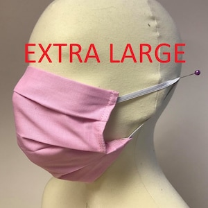 May include: A light pink, pleated face mask with white elastic ear loops. The mask is labeled "EXTRA LARGE" in red text. A pin is used to secure the elastic on the side of the mask.