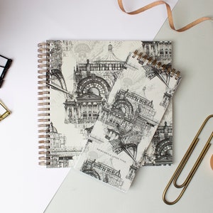 May include: Two spiral bound notebooks with a black and white illustration of buildings on a white background. The smaller notebook has the text "Newcastle upon Tyne" printed on the cover.