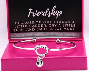 May include: A silver friendship bracelet with a knot charm and a small charm that says "Bff". The bracelet is in a pink box with a floral design and the text "Friendship Because of you, I laugh a little harder, cry a little less, and smile a lot more."