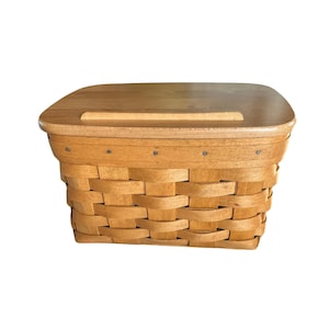 May include: A rectangular, light brown woven basket with a wooden lid. The basket is made of woven strips of wood, and the lid has a handle. The basket is designed for storage and decorative purposes.