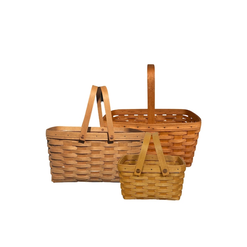 May include: Three woven baskets of varying sizes. The largest basket has a rectangular shape with a wooden handle. The middle basket has a rectangular shape with a wooden handle. The smallest basket has a rectangular shape with a wooden handle.