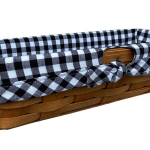 May include: A rectangular woven basket with a black and white gingham fabric lining. The basket is made of light brown wood and has a handle on each side. The fabric is tied in a bow on each side.