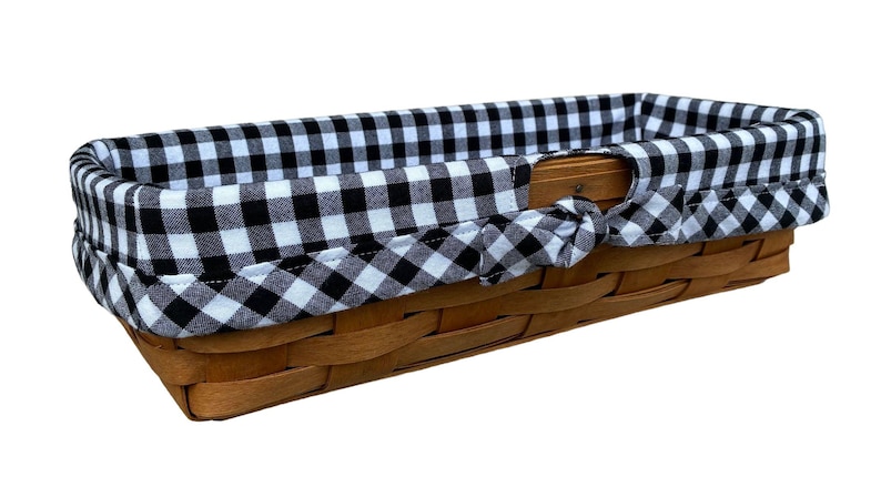 May include: A rectangular woven basket with a black and white gingham fabric lining. The basket is made of light brown wood and has a handle on each side. The fabric is tied in a bow on each side.