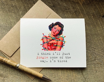 Könnte beinhalten: Eine weiße Grußkarte mit einer Illustration im Vintage-Stil, die eine Person zeigt, die in bunte Lichterketten eingewickelt ist. Der Text lautet: i think i'll just jingle some of the way. i'm tired. Das Wort jingle ist in Rot gedruckt.