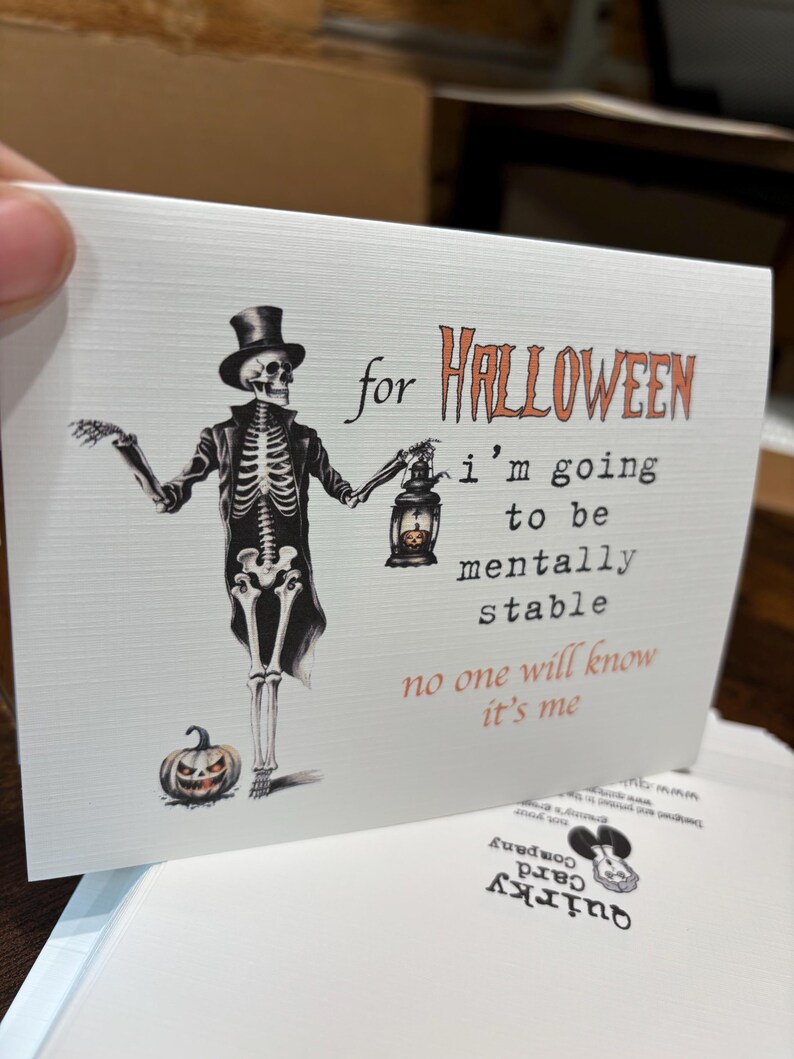 May include: A white greeting card featuring a skeleton wearing a top hat and coat, holding a lantern with a small pumpkin inside. Text reads: for HALLOWEEN i'm going to be mentally stable no one will know it's me. A small jack-o'-lantern sits at the feet.