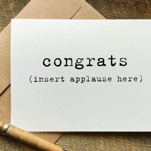 May include: A white card with black text that reads "congrats (insert applause here)".