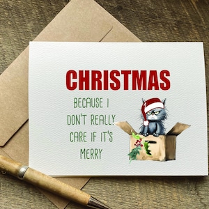 May include: A Christmas card with a grumpy cat wearing a Santa hat sitting in a box. The text on the card reads "Christmas because I don't really care if it's merry."