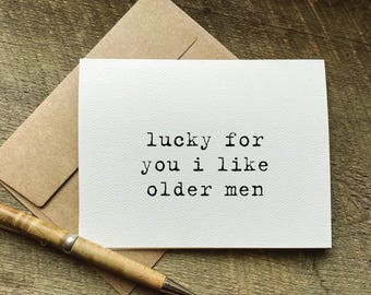 May include: A white greeting card with the text "lucky for you I like older men" in black typewriter font. The card is on a wooden surface with a brown envelope and a pen.