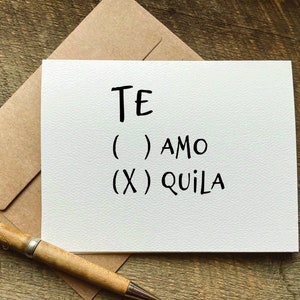 May include: White card with black text that reads "TE ( ) AMO (X) QUIILA".