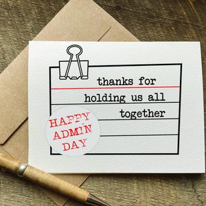 May include: A white card with black text that reads "thanks for holding us all together". A red and white circle sticker with the text "HAPPY ADMIN DAY" is on the card.