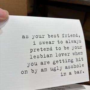 May include: A white rectangular greeting card with black typewriter-style text that reads: as your best friend, i swear to always pretend to be your lesbian lover when you are getting hit on by an ugly asshole in a bar. The card has a textured finish.