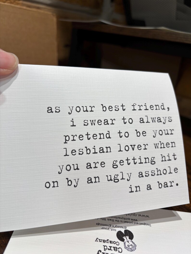 May include: A white rectangular greeting card with black typewriter-style text that reads: as your best friend, i swear to always pretend to be your lesbian lover when you are getting hit on by an ugly asshole in a bar. The card has a textured finish.