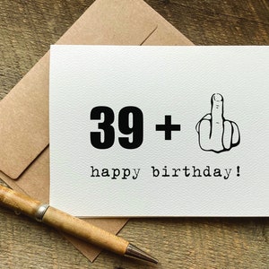 May include: A white card with black text that reads "39 +" and a black and white illustration of a middle finger. The text "happy birthday!" is also printed in black.