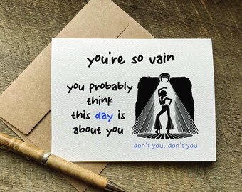 Puede incluir: Una tarjeta de felicitación blanca con el texto "you're so vain, you probably think this day is about you." Una silueta negra de una persona bailando bajo un foco de luz está a la derecha. Un bolígrafo y un sobre están en el fondo.
