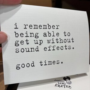 May include: A white rectangular greeting card with a textured surface featuring black typewriter-style text that reads: i remember being able to get up without sound effects. good times. The card has a clean, minimalist design with black lettering.