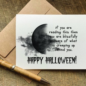 May include: A white card with a black and white illustration of a crescent moon with clouds. The card has the text "if you are reading this then you are blissfully unaware of what is creeping up behind you. HAPPY HALLOWEEN!"