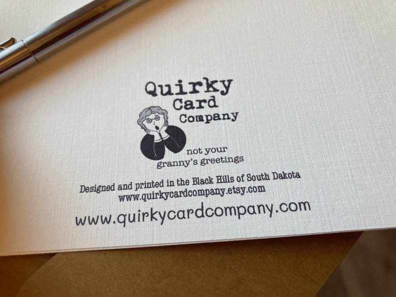 Może przedstawiać: Logo firmy Quirky Card Company z kresk&oacute;wkową ilustracją kobiety ze zdziwionym wyrazem twarzy. Tekst głosi "not your granny's greetings". Strona internetowa firmy to www.quirkycardcompany.com.